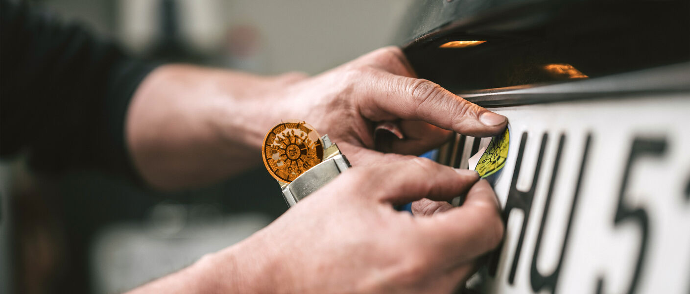 GTÜ Prüfingenieur klebt HU-Plakette am Kennzeichen
